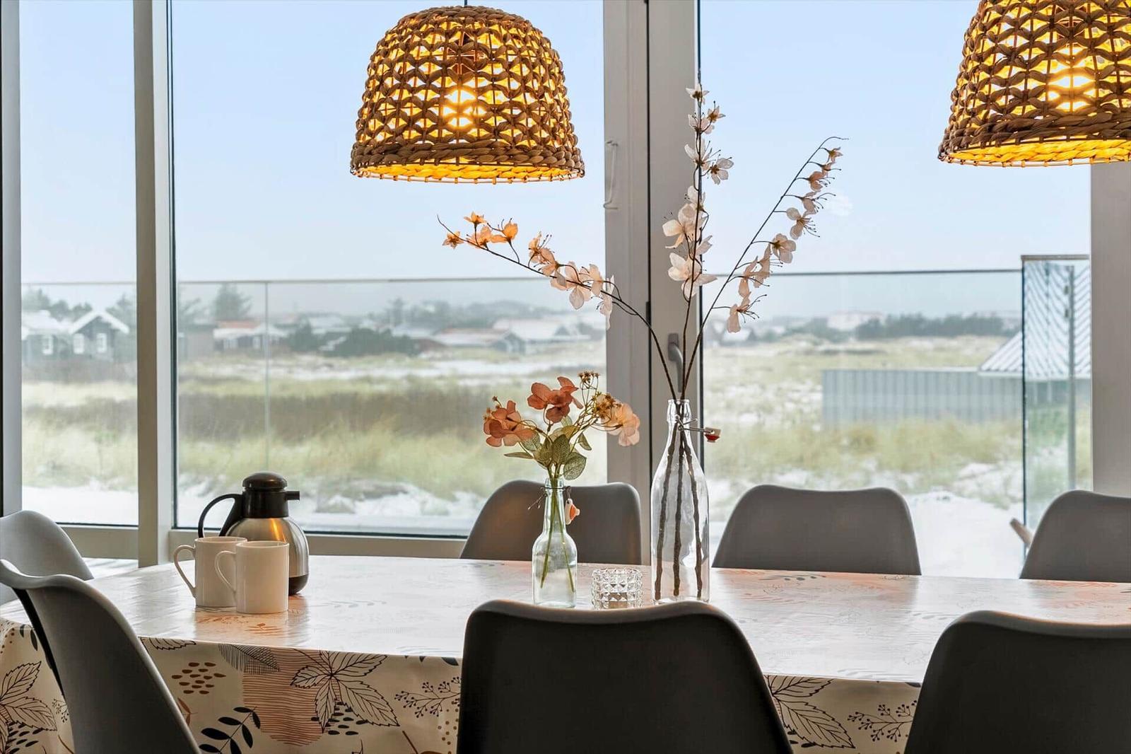 Esstisch mit Stühlen, Vasen und Decke vor großem Fenster mit Blick auf Landschaft.