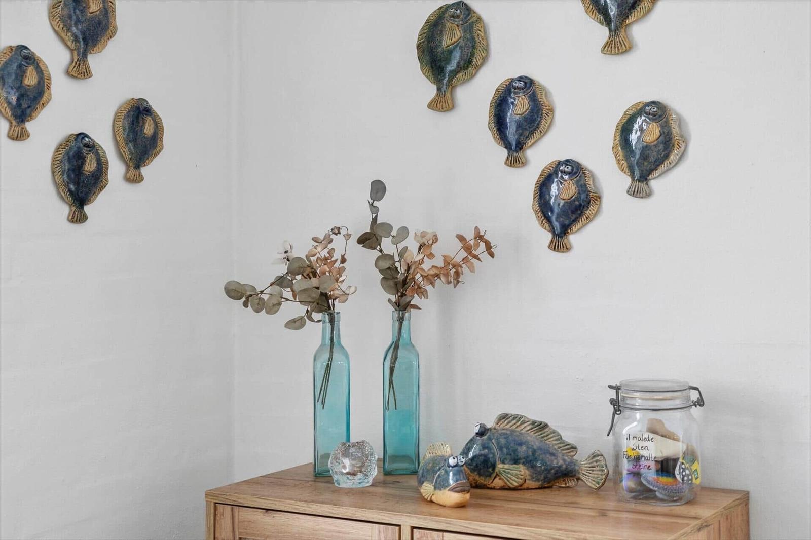 Wand mit Fischdekoration, Holzschrank mit Vasen und Glasbehälter.