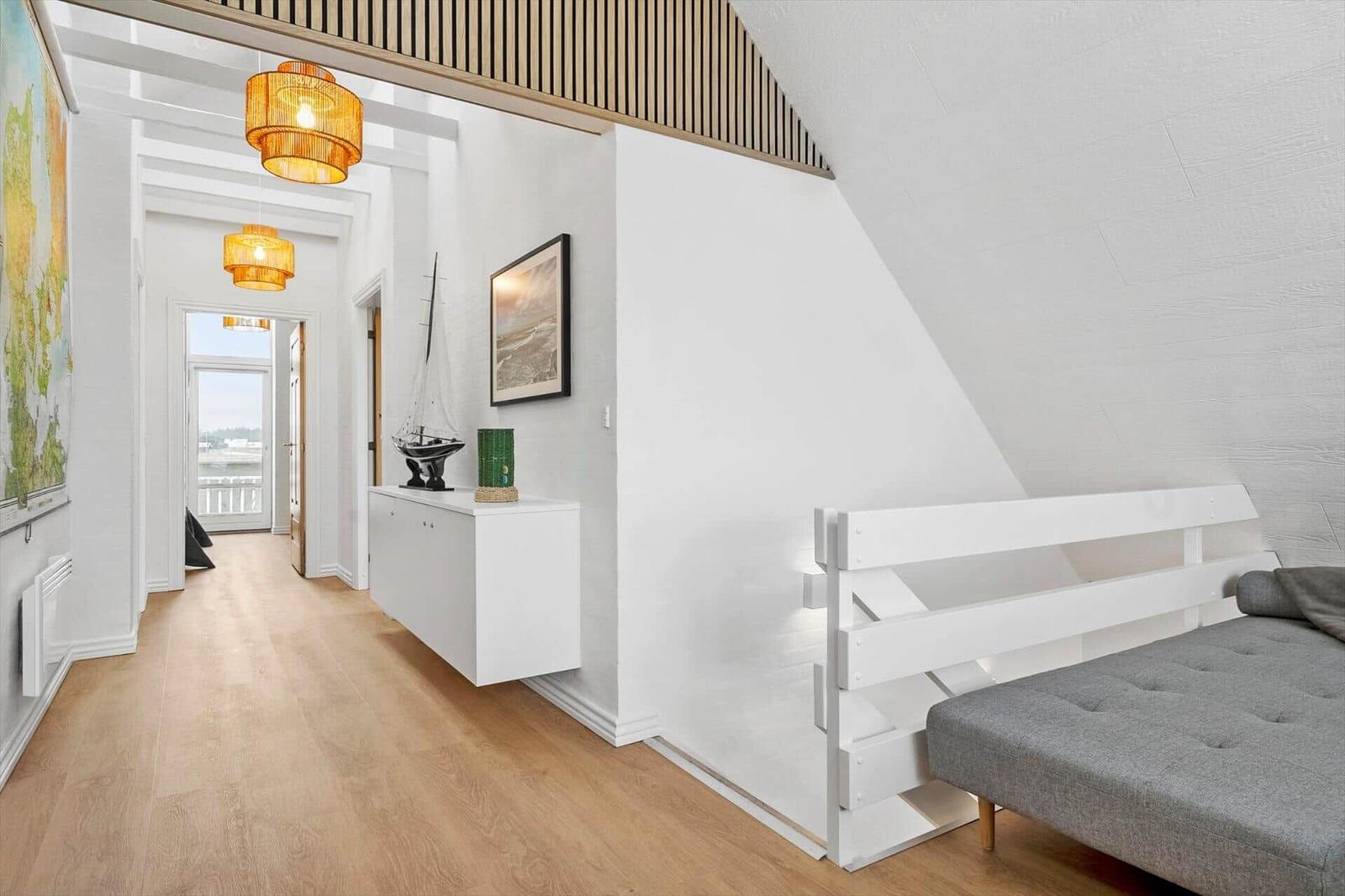 Flur mit weißer Wand, Holzboden und Bett unter Dachschrägen.