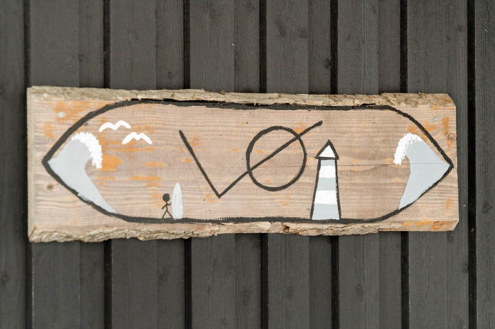 Holzschild mit Strandmotiv und Leuchtturm, an dunkler Holzwand angebracht.