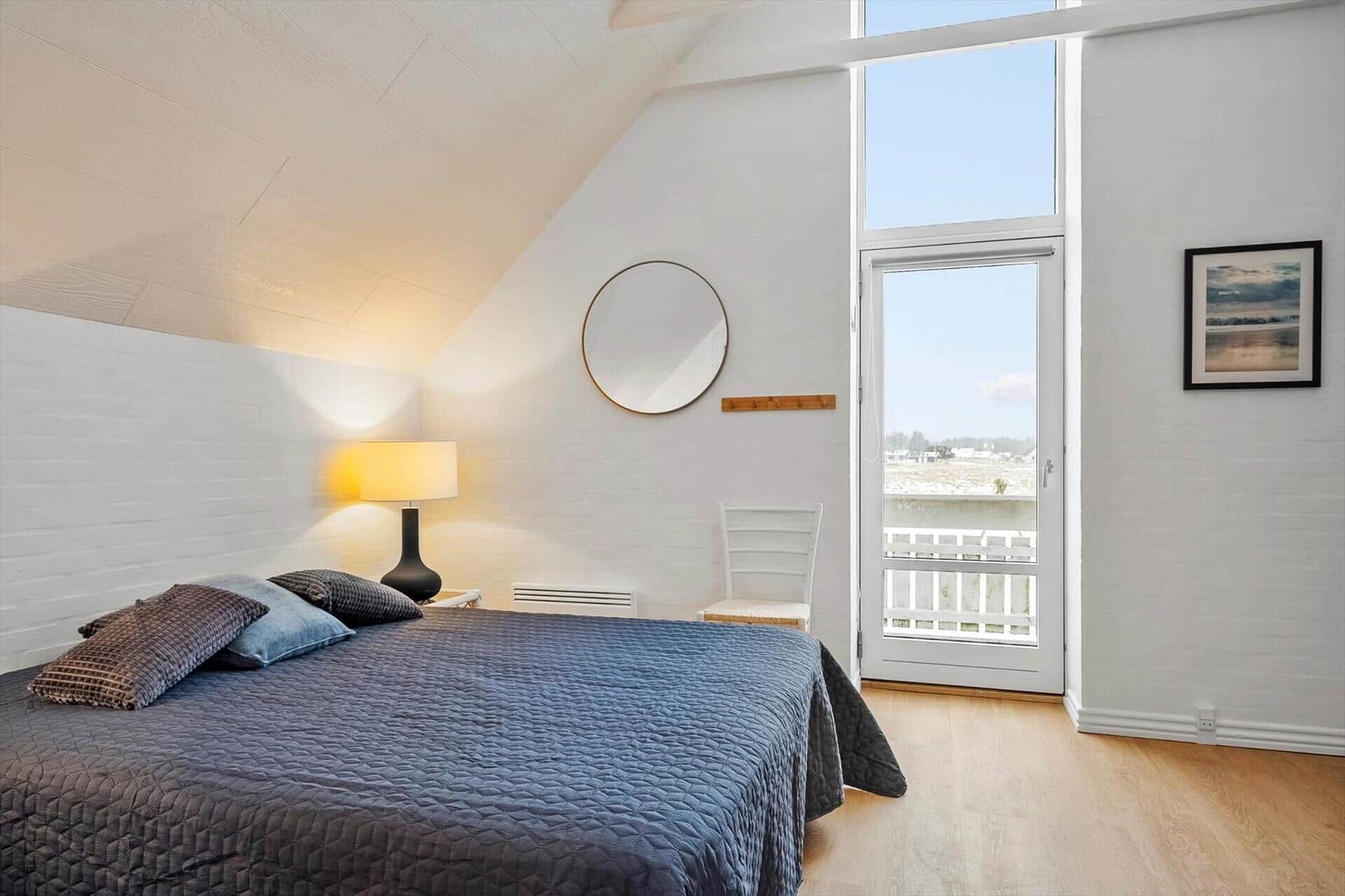 Schlafzimmer mit Dachschräge, Bett, Lampe, Spiegel und Balkontür.