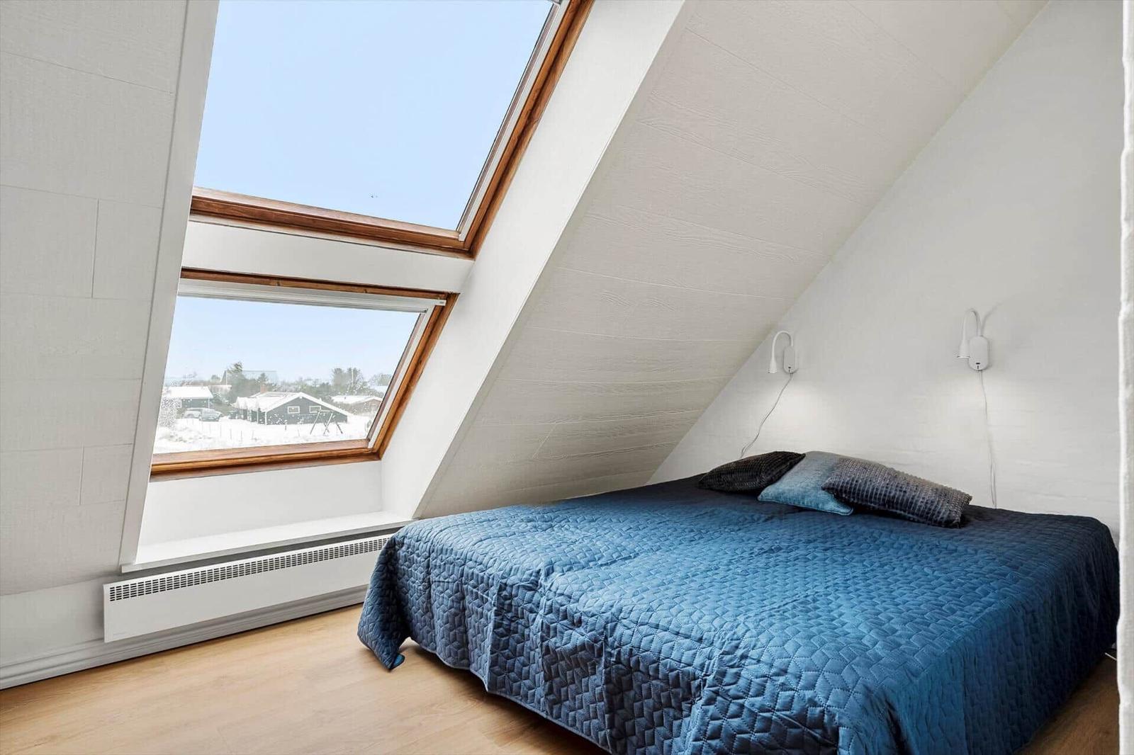 Schlafzimmer mit Dachfenster und blauer Bettdecke.
