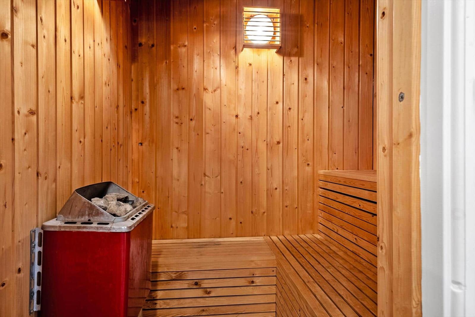 Sauna mit Holzwand und Sitzbank, roter Ofen und Wandlampe.