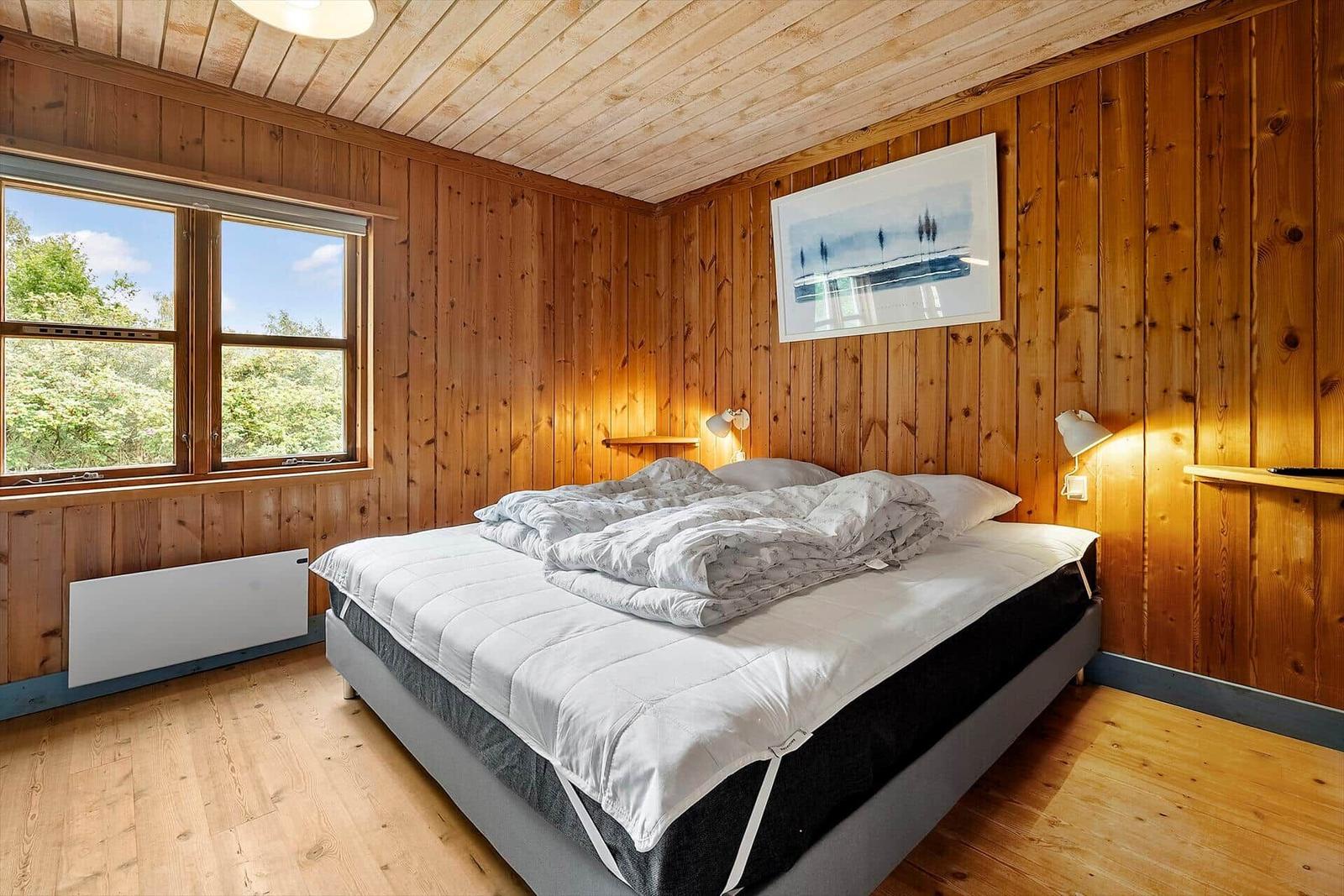 Bedroom with wooden walls, bed, and window view of trees
