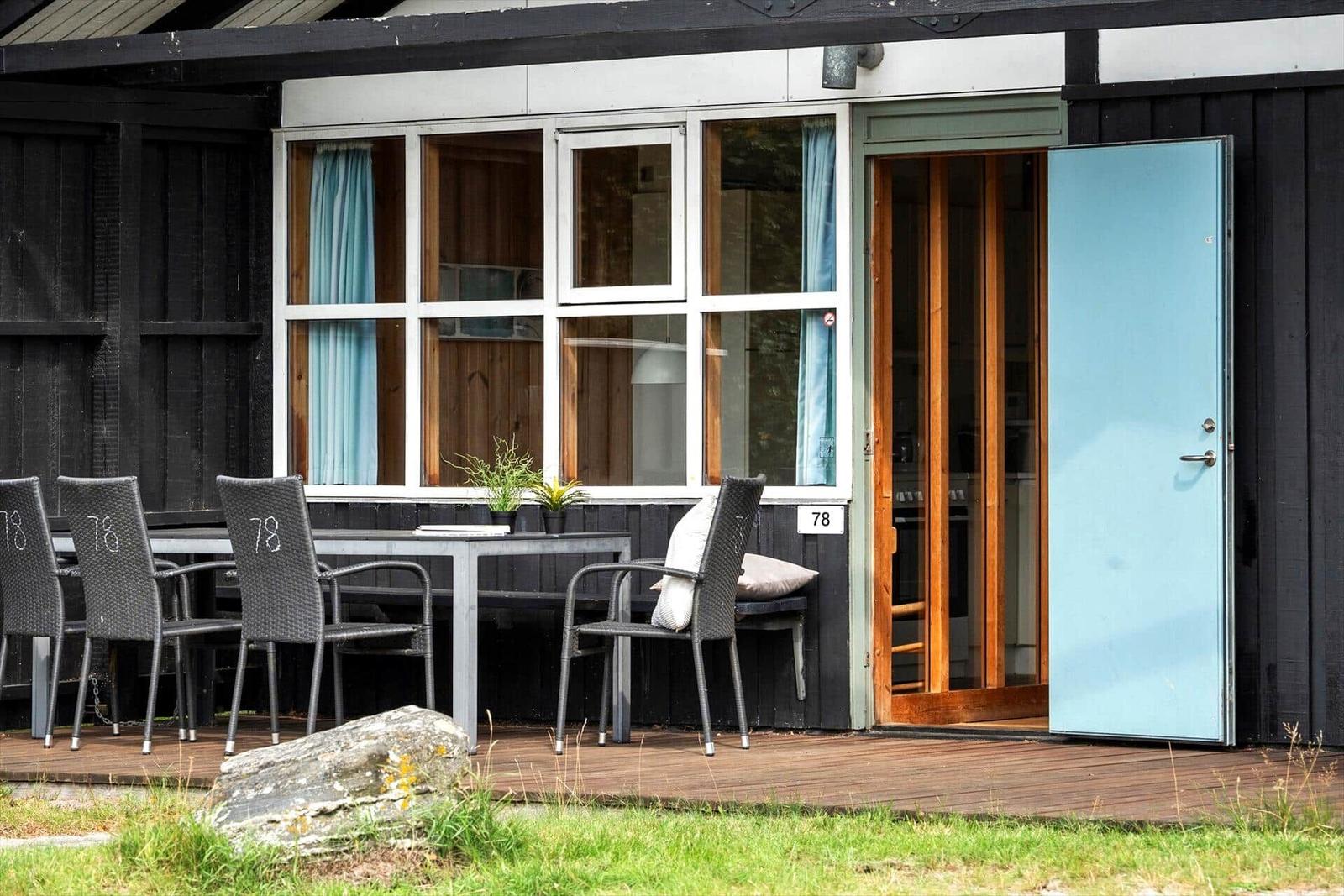 House with terrace, table, chairs, and blue door. Windows with light blue curtains.