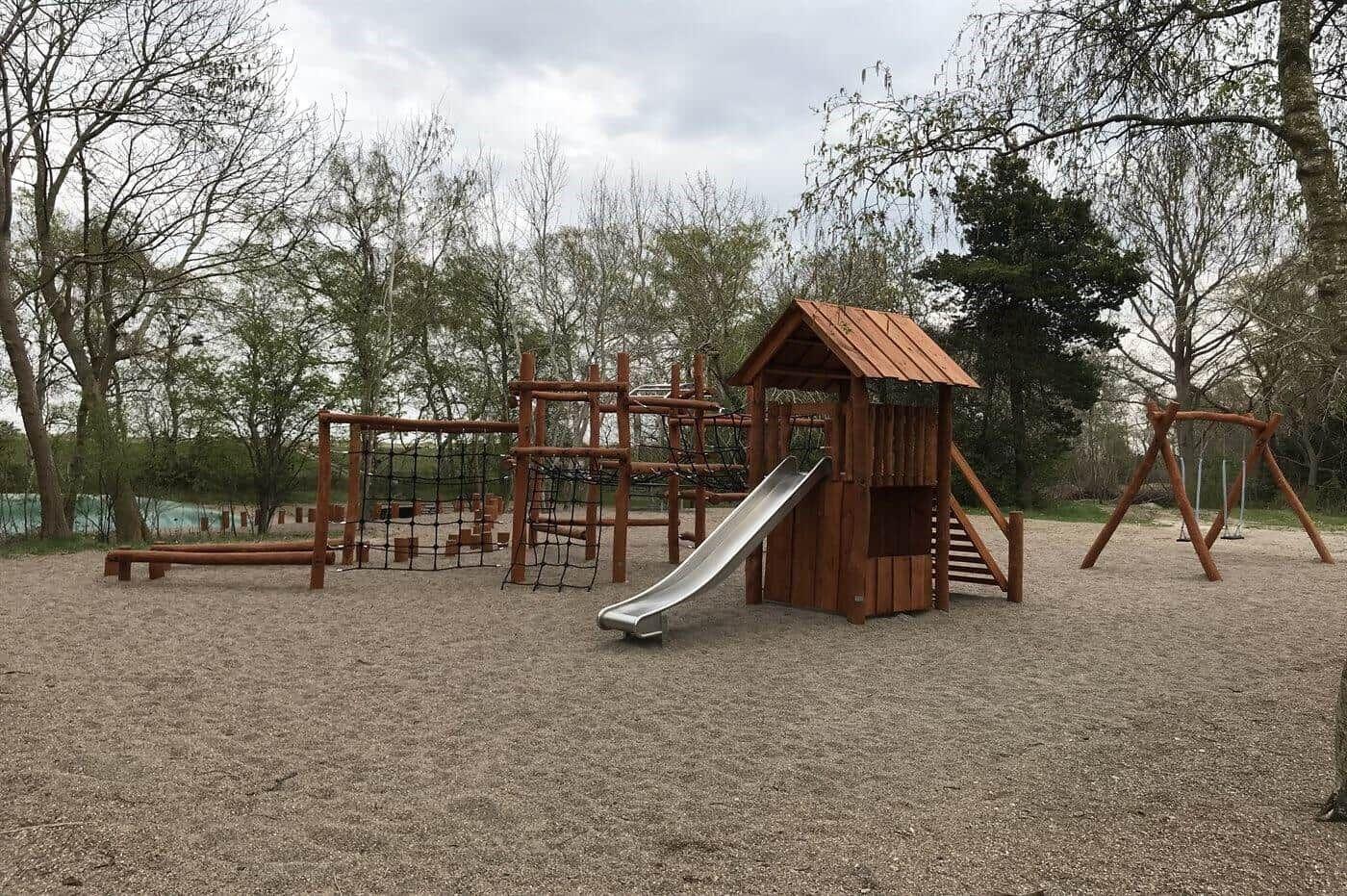 Wooden playground with slide, climbing frame, and swing on gravel surface