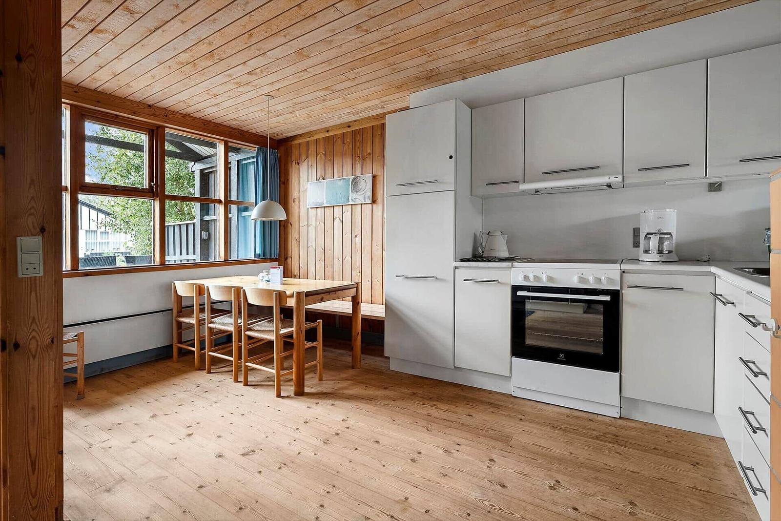 Kitchen with dining area, wooden ceiling and windows. White cabinets and wooden furniture.