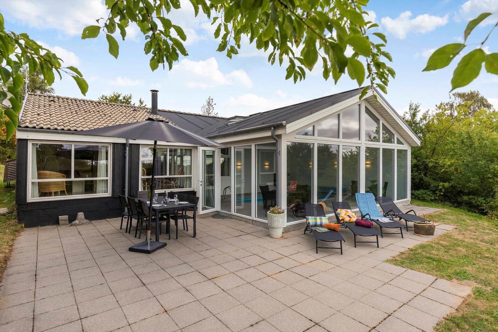 Haus mit großem Terrassenbereich, Sonnenliegen und Gartentisch unter einem Sonnenschirm.