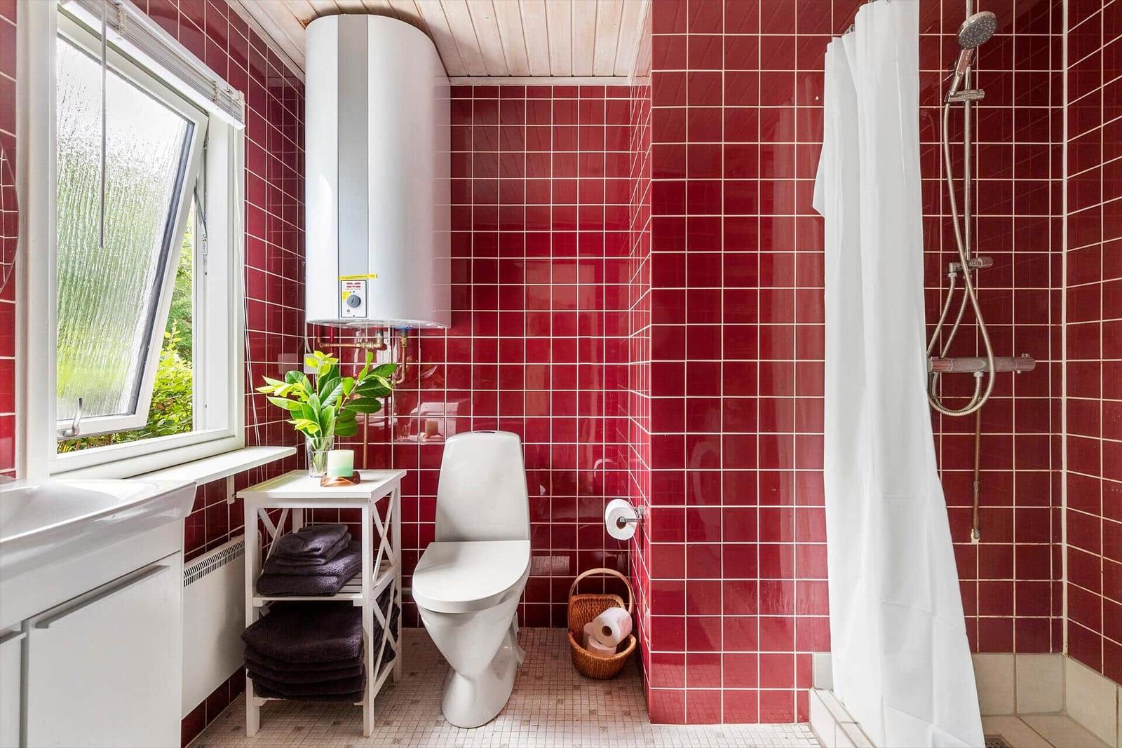 Bathroom with red tiles, shower, toilet, and window.