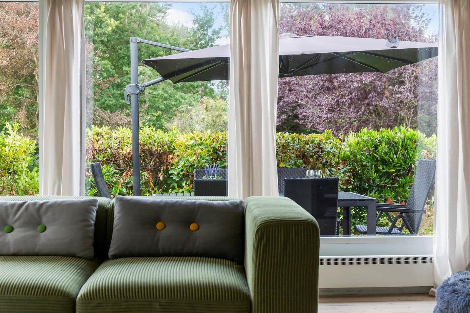 Green sofa with cushions overlooks terrace with umbrella and garden.