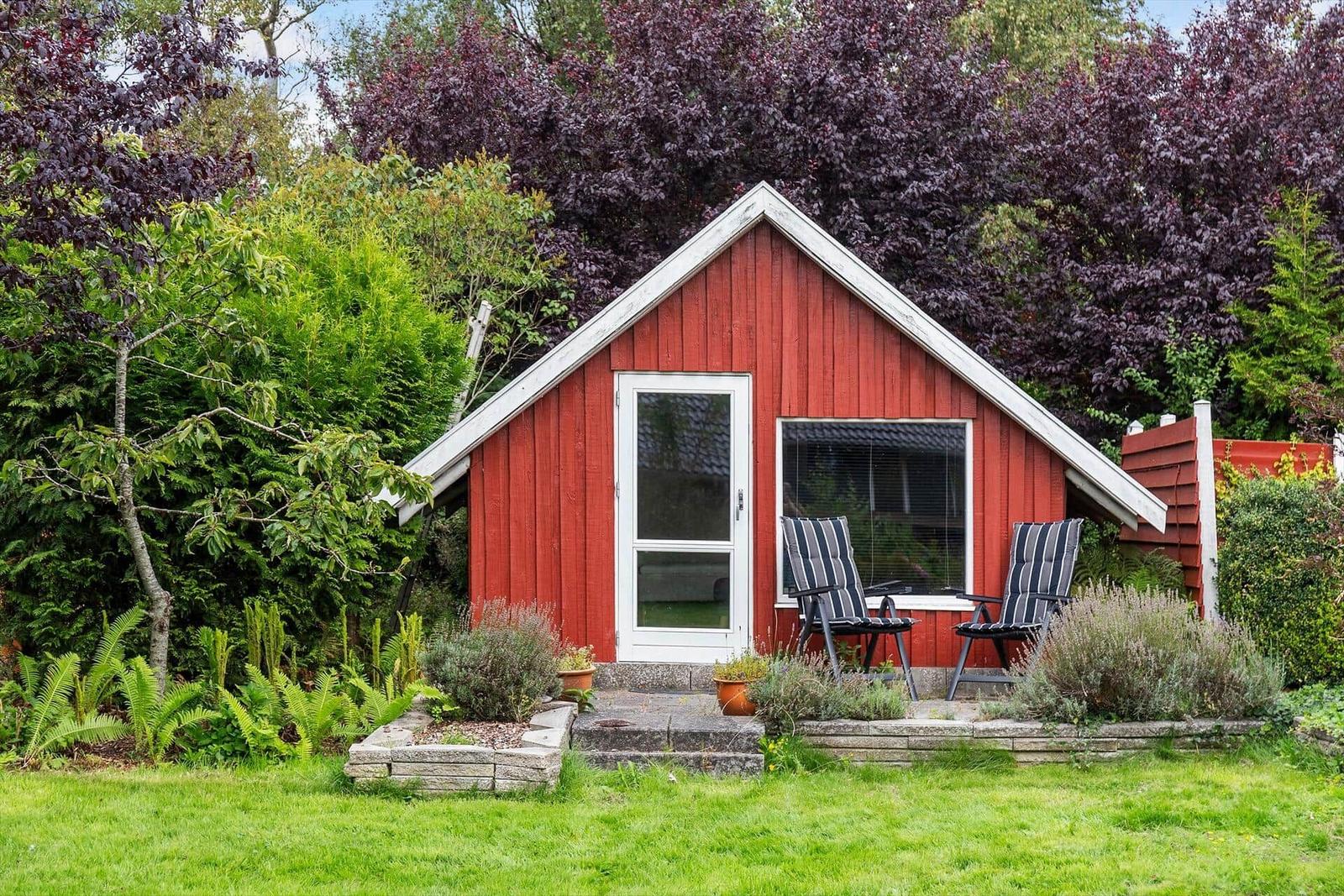 Red wooden house with terrace and chairs in the garden