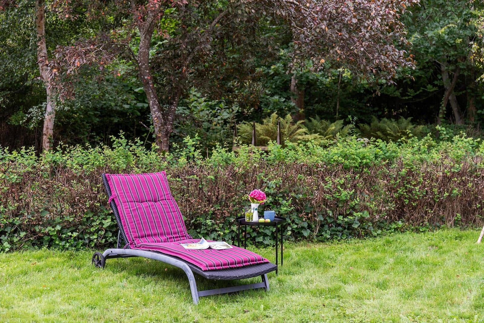 Lounger with stripes on lawn, small table with flowers and drinks.