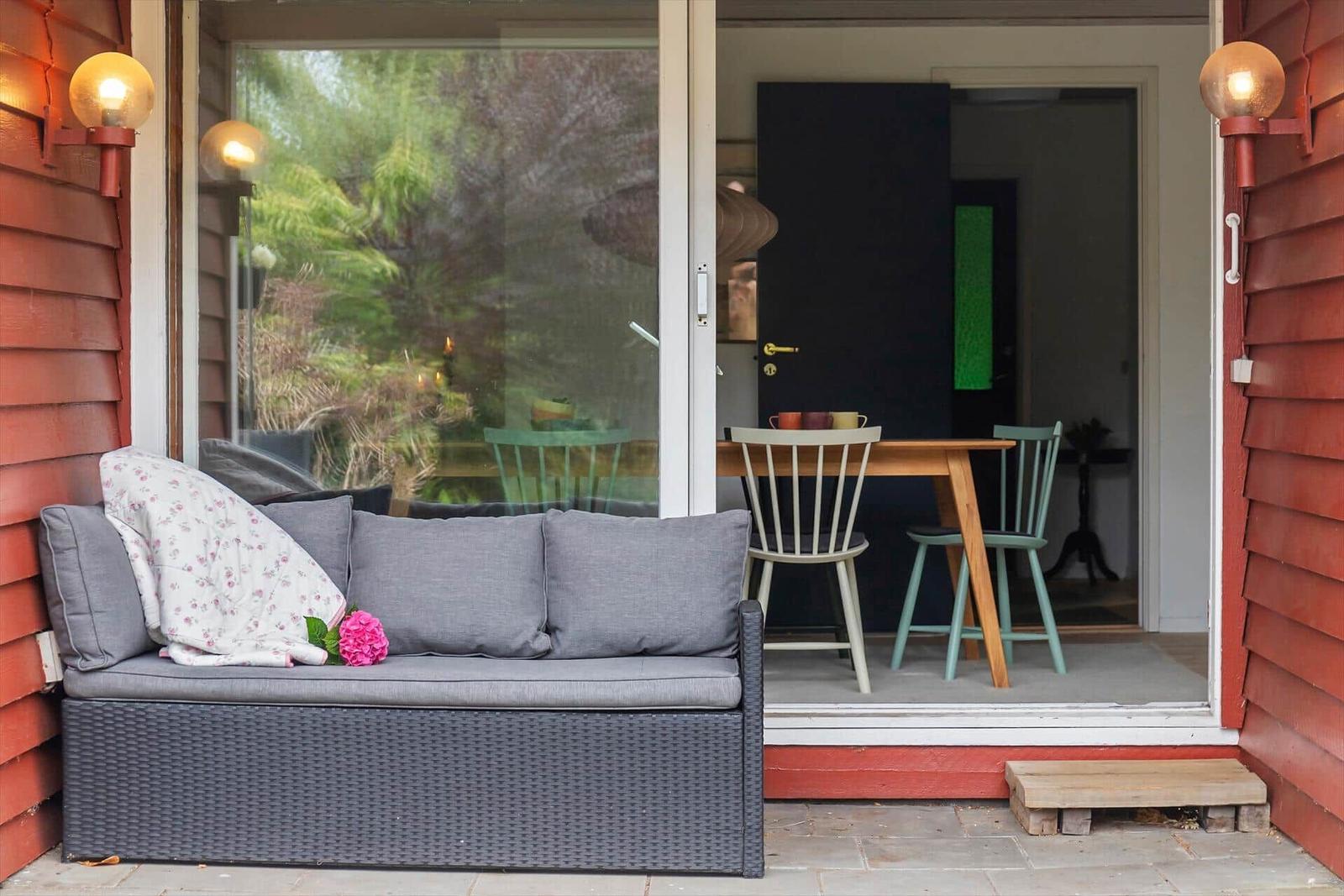 Patio with gray sofa, table and chairs. Red wooden frame and outdoor lighting.
