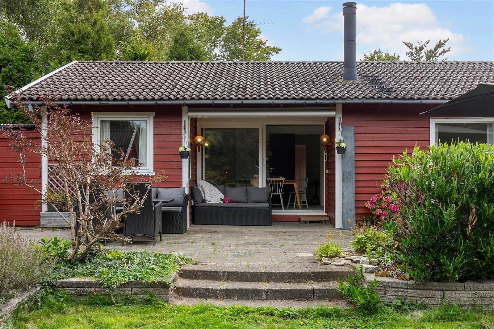 Red wooden house with terrace and garden. Glass door leads inside.