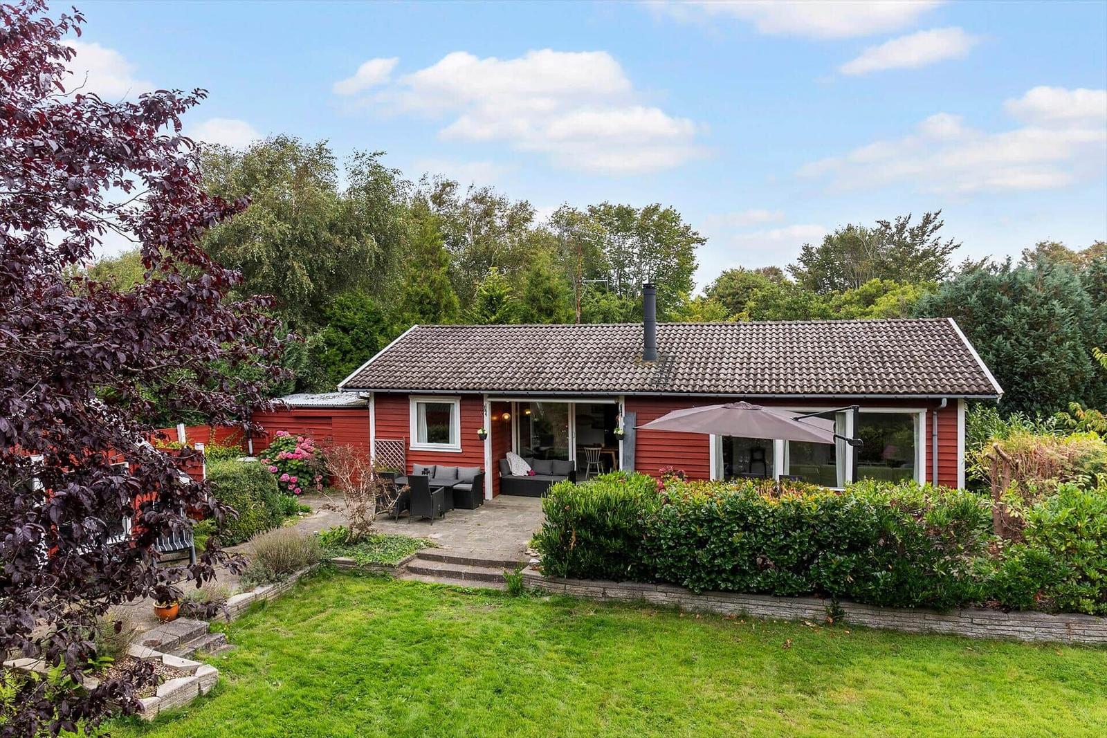 Red house with terrace, garden, and view into the woods.
