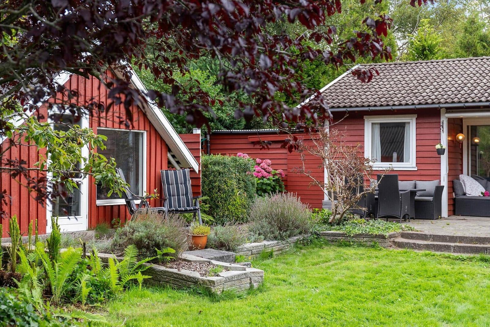 Red wooden house with garden and terrace with seating.