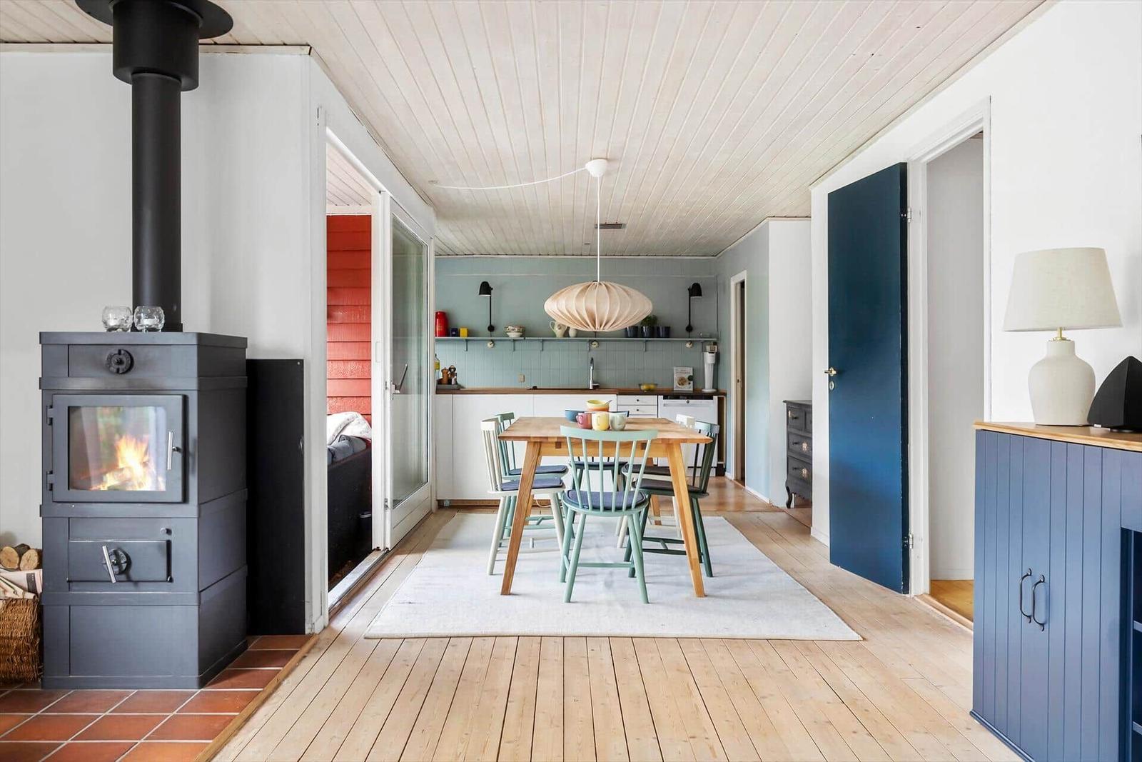 Kitchen with dining table, wooden floor, and wood-burning stove in living area.