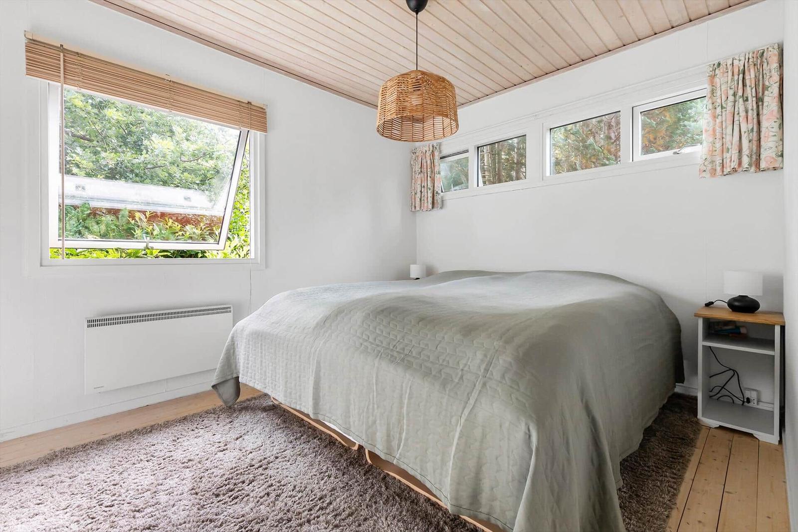 Bedroom with bed, windows, and wooden ceiling.