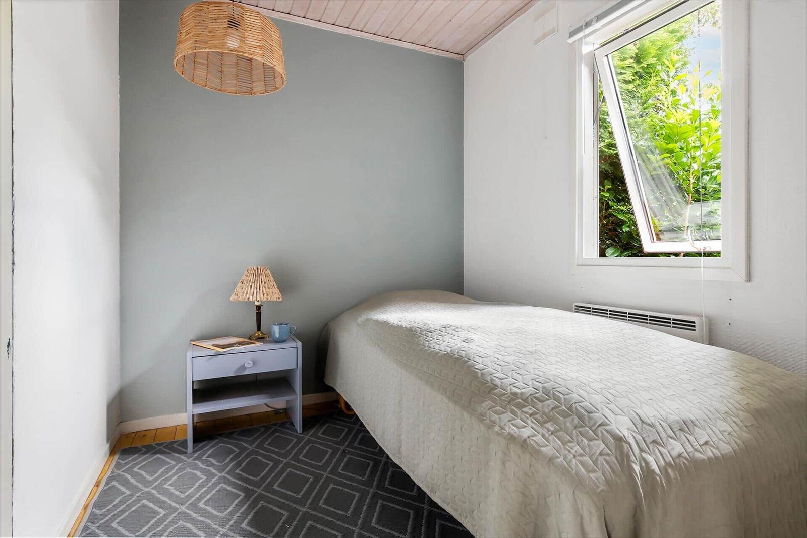 A bedroom with bed, nightstand, and window with view of greenery.