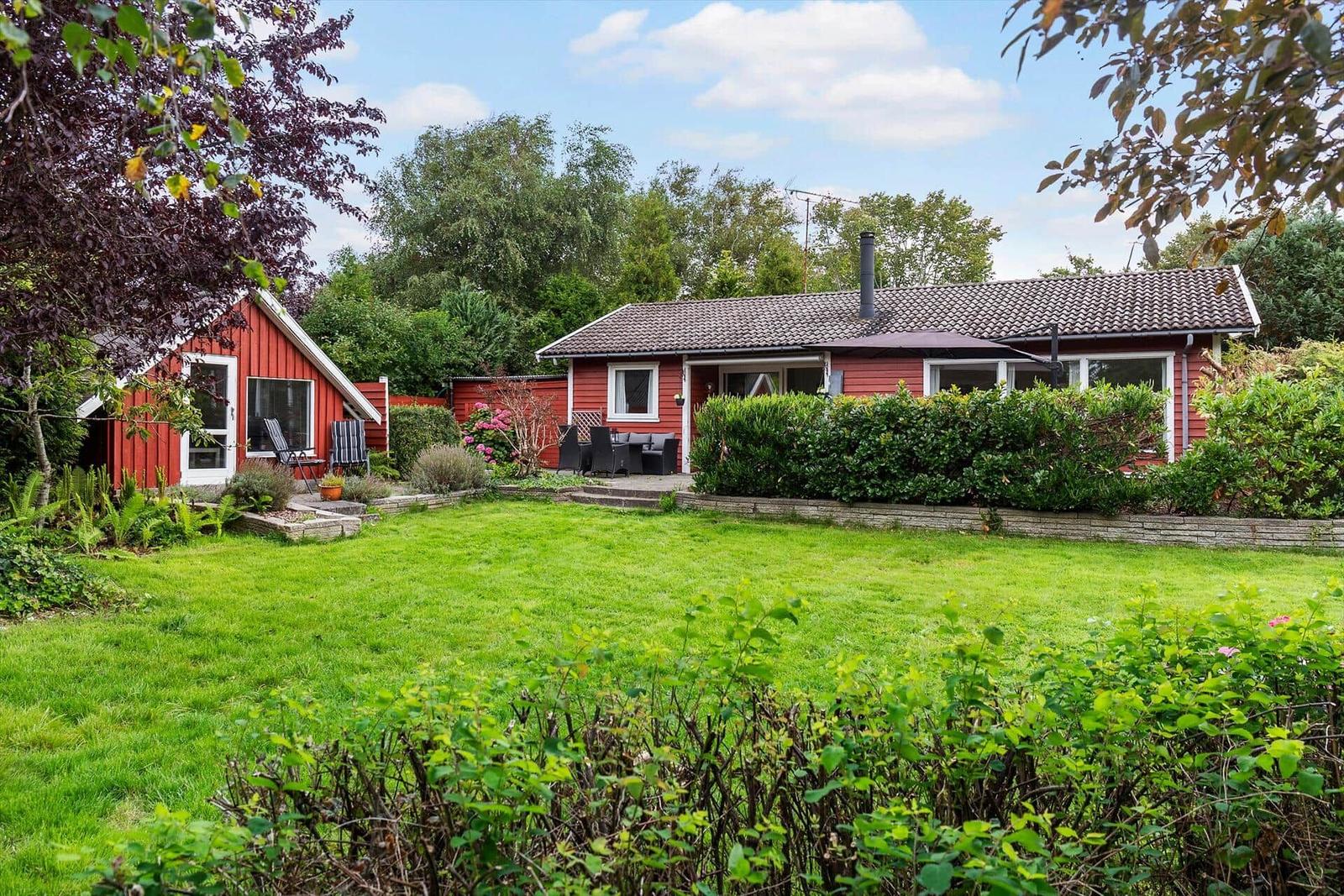 Red house with garden and terrace. Surrounded by trees and shrubs.