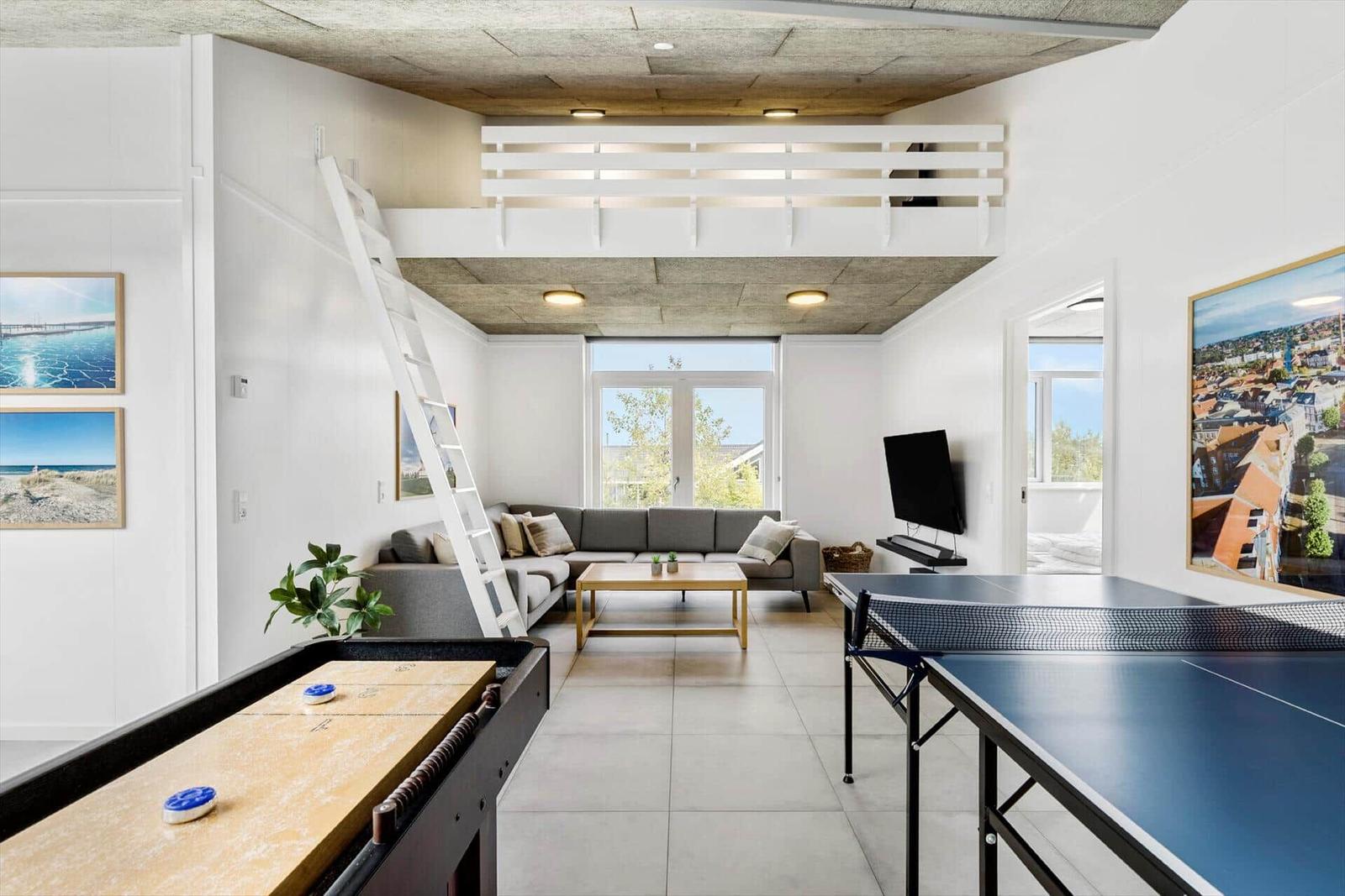 Wohnbereich mit Sofa, Tischtennisplatte und Klettertreppe zu einer oberen Ebene.