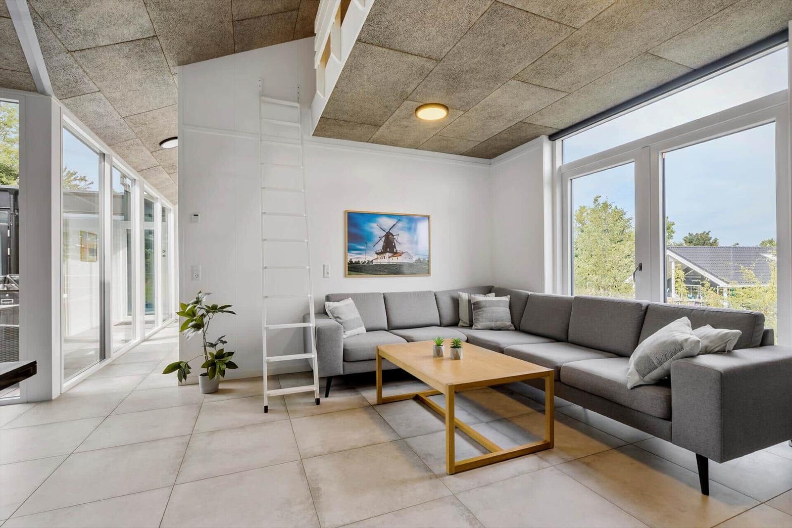Wohnzimmer mit grauem Sofa, Holztisch und großen Fenstern.