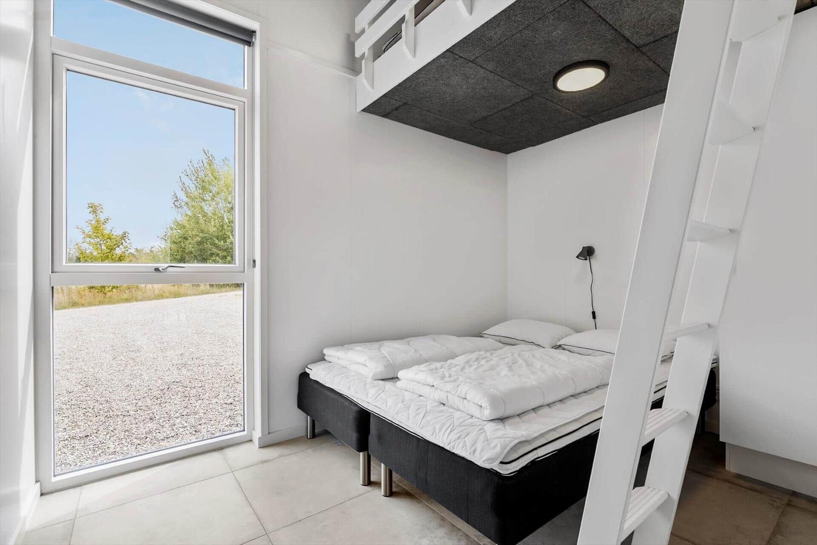 Zimmer mit Doppelbett, Fenster und oberem Schlafbereich mit Leiter.