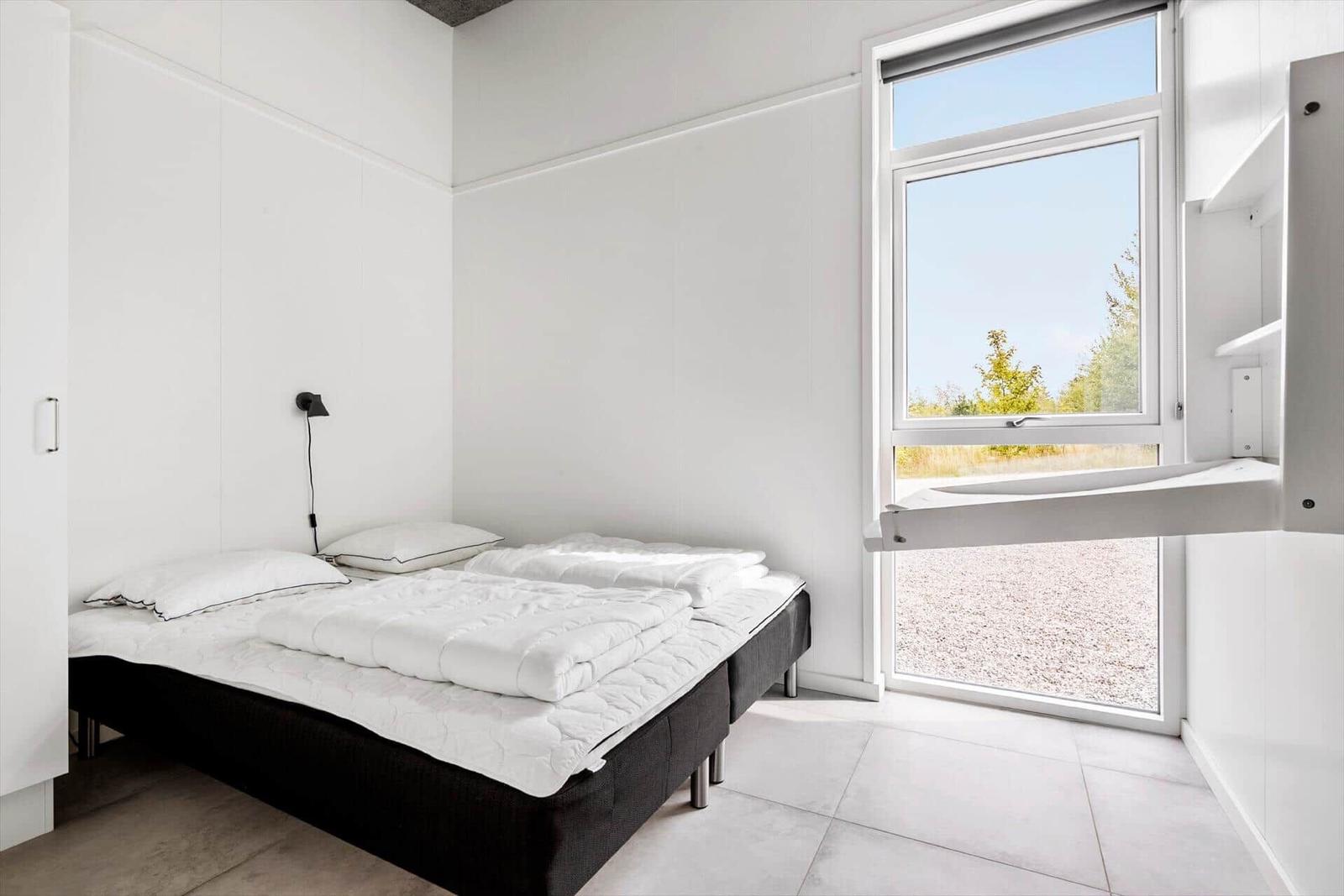 Schlafzimmer mit weißem Bett und großem Fenster zur Außensicht.