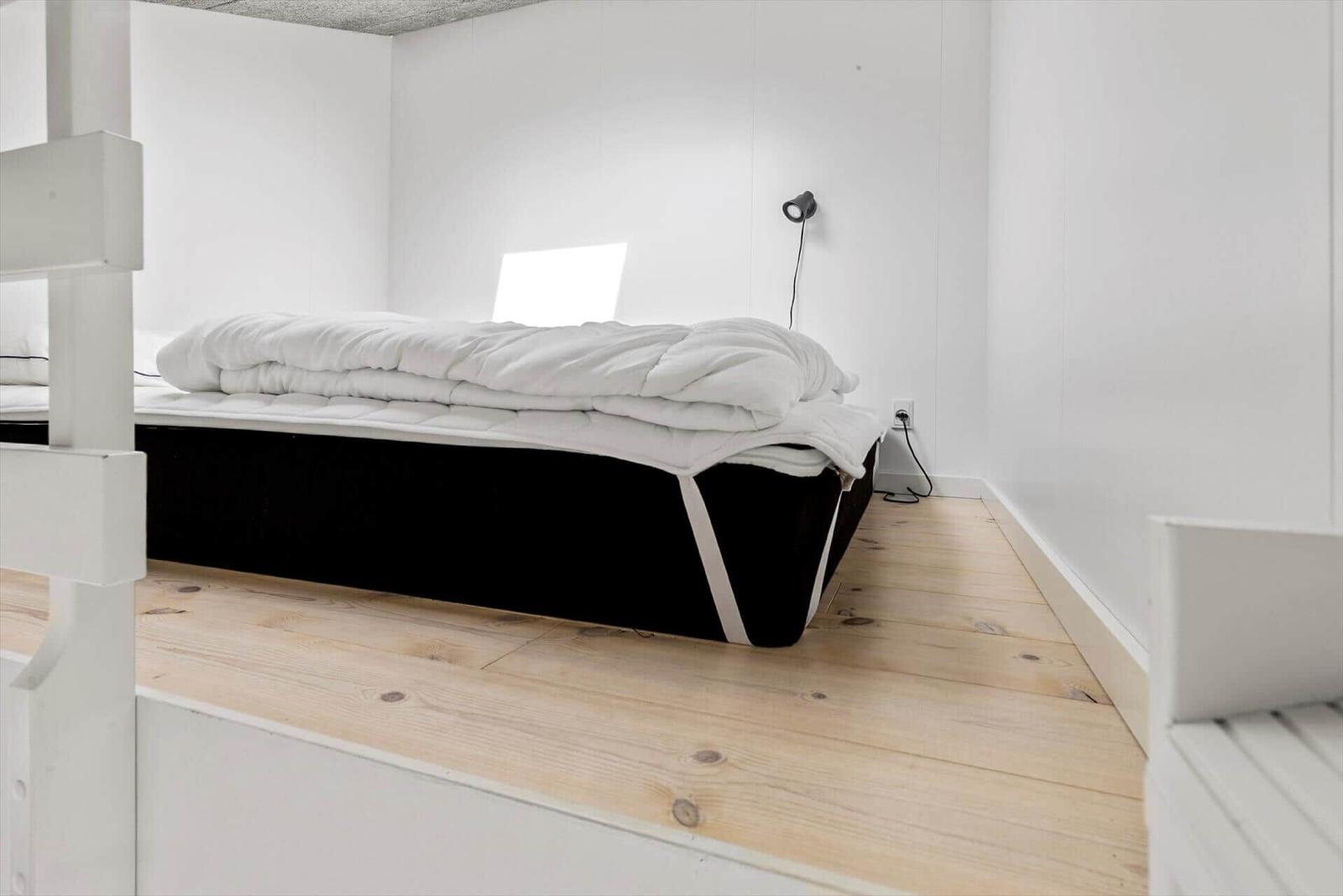Schlafzimmer mit Bett, Holzboden und Wandbeleuchtung.