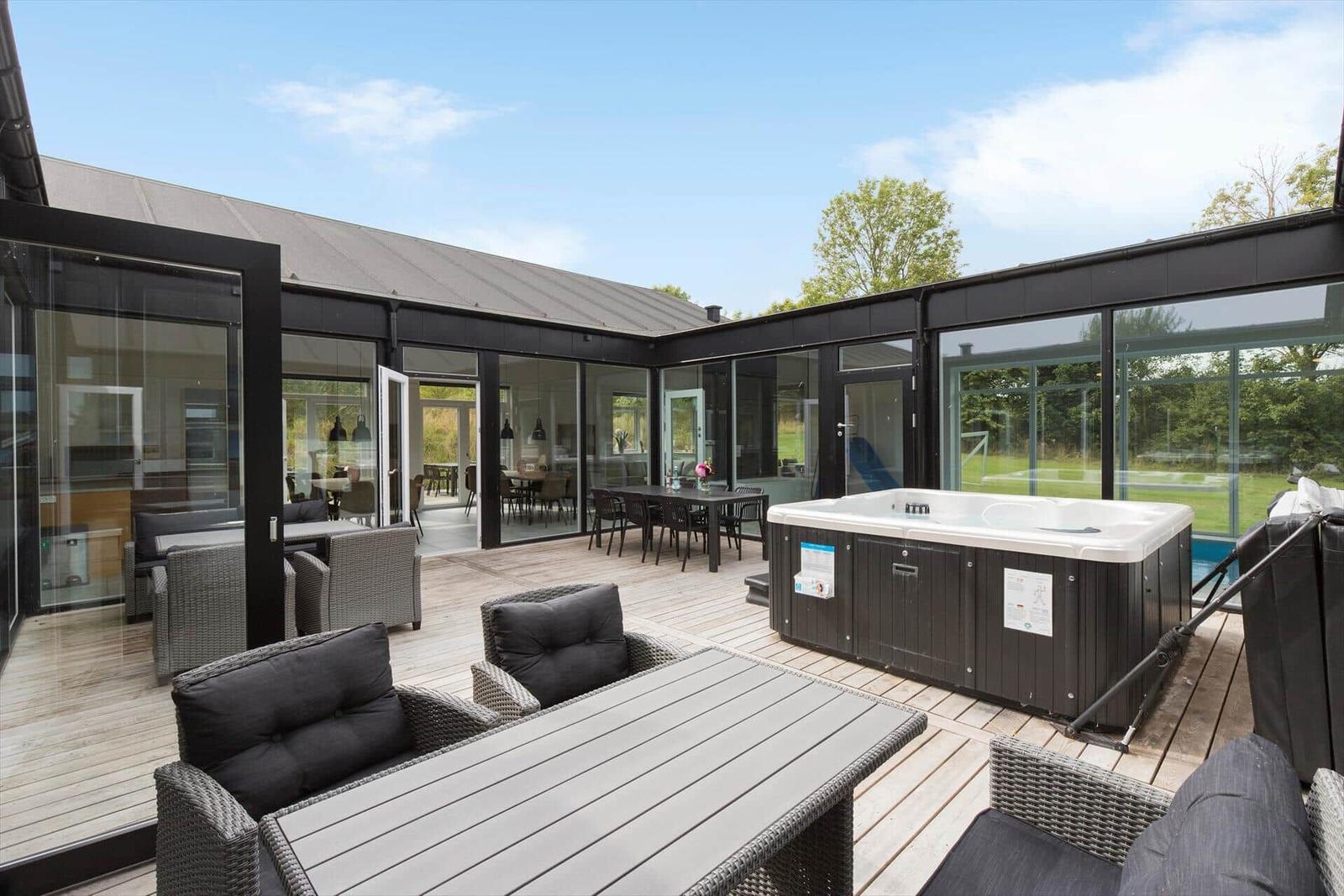 Terrasse mit Sitzgelegenheiten und Whirlpool. Glasfassade führt in das Innere.