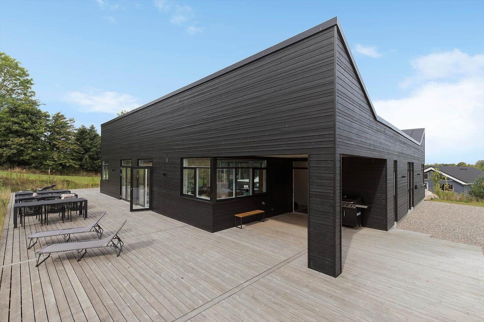Moderne schwarze Villa mit großem Holzterrasse, Grillbereich und Außensitzgelegenheiten.