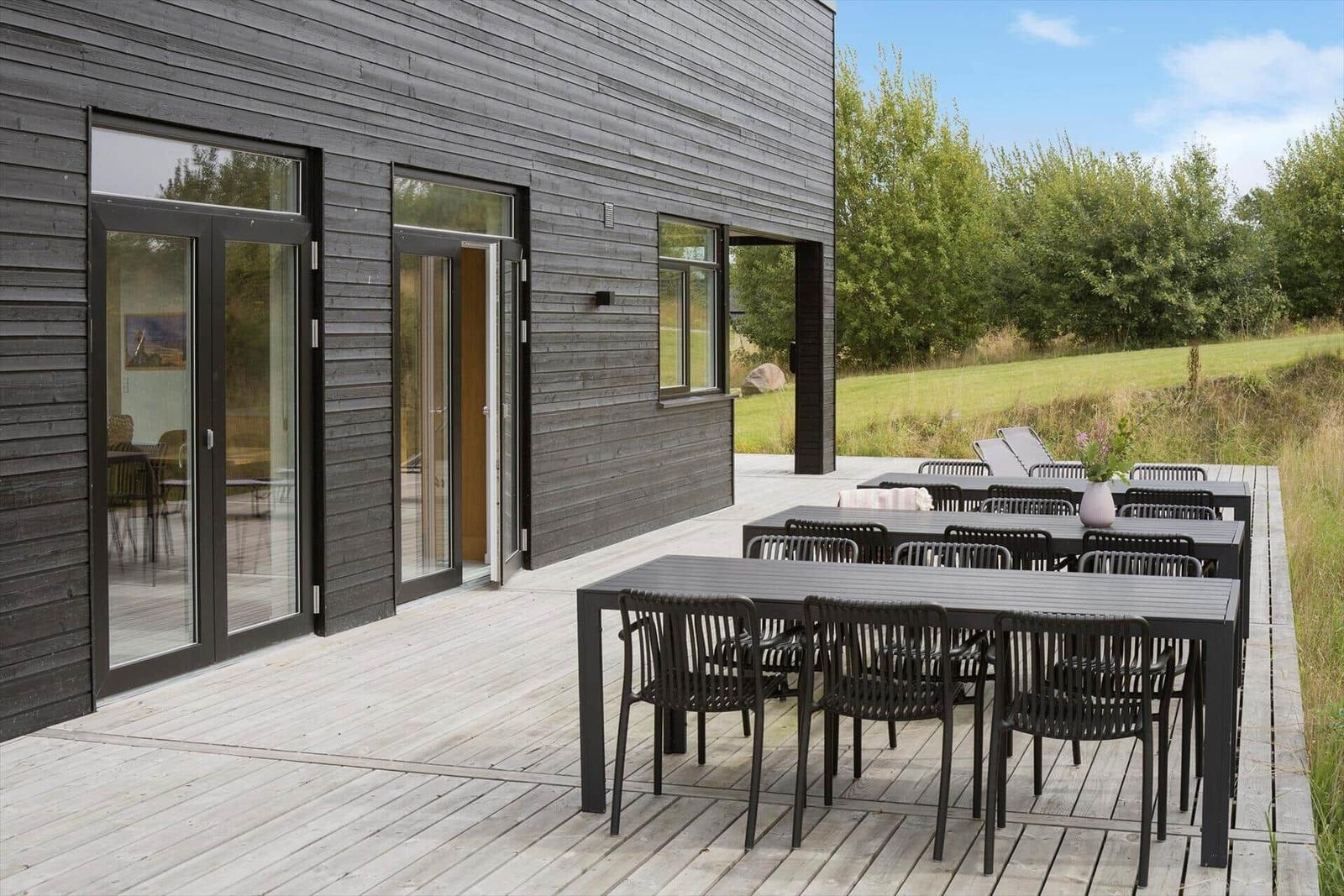 Terrasse mit Tischen und Stühlen vor modernem Haus mit Holzfassade.