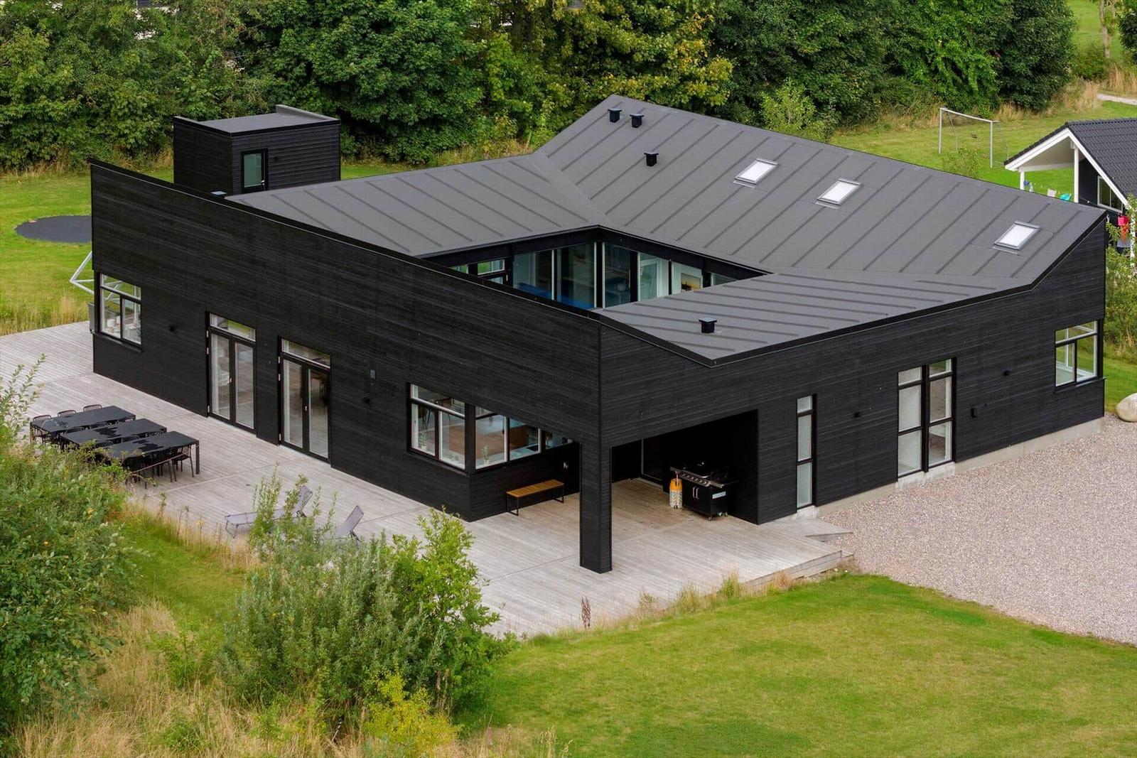 Moderne schwarze Villa mit großem Holzdeck und Garten.
