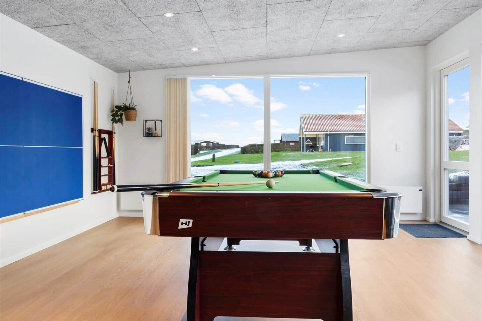 Raum mit Billardtisch und Tischtennisplatte, großes Fenster mit Blick auf Garten.