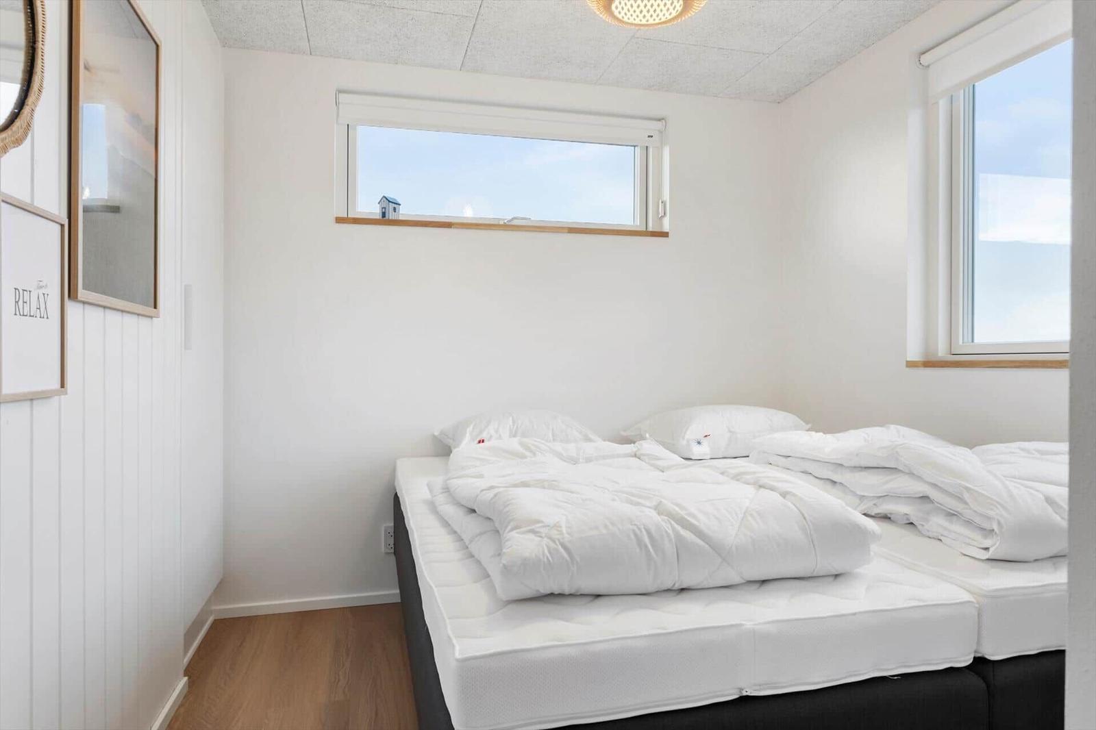 Schlafzimmer mit weißem Bett, Fenstern und Wandbildern.