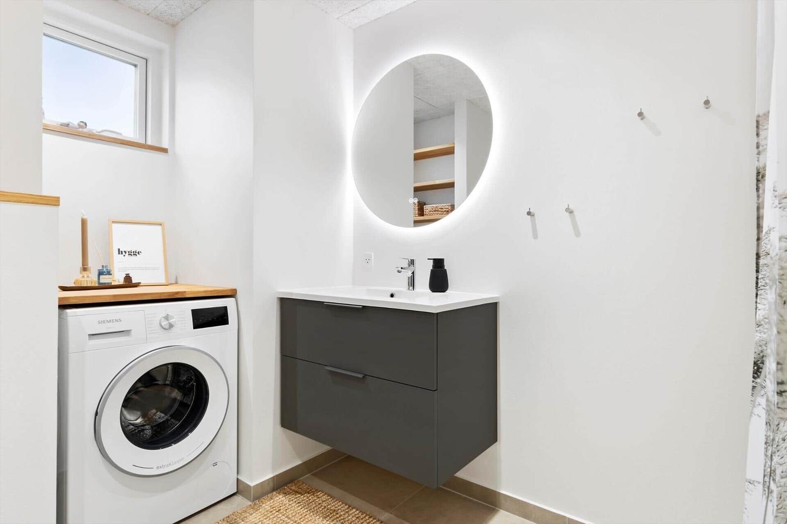 Badezimmer mit Waschmaschine, Spiegelschrank und Fenster.