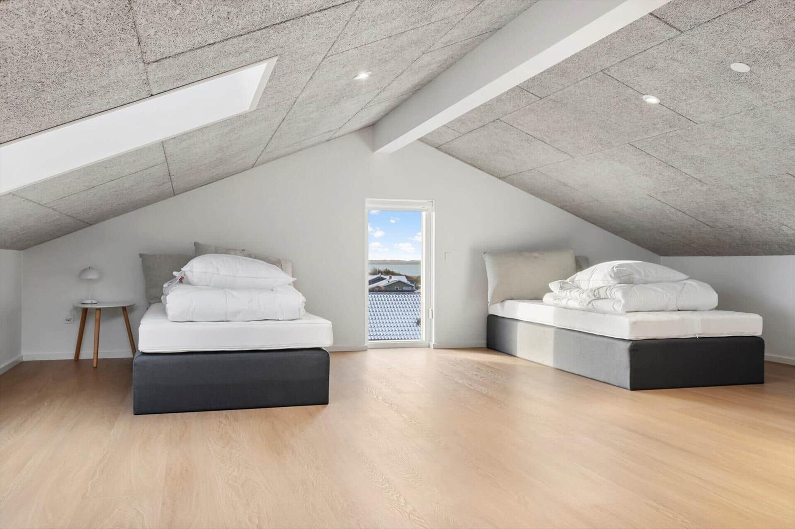 Zwei Betten in einem Dachzimmer mit Holzboden und Fensterblick.