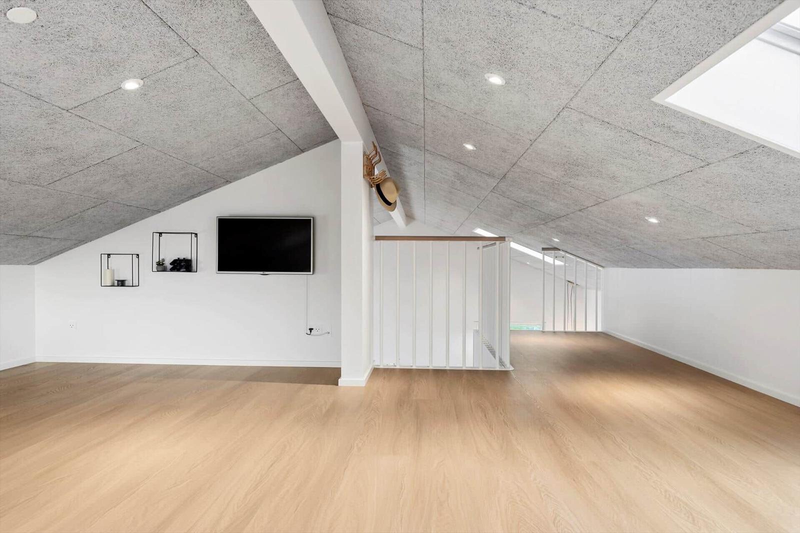 Dachgeschosszimmer mit Holzboden, Fernseher und Schränken an der Wand.