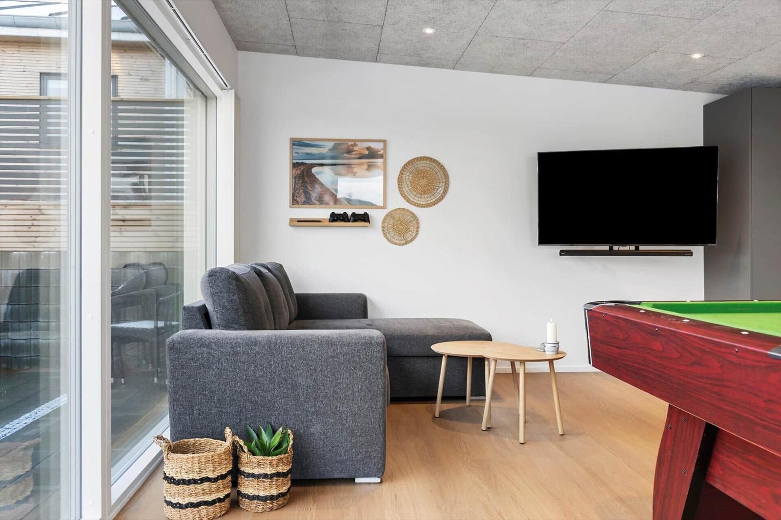 Wohnzimmer mit Sofa, Fernseher und Billardtisch. Große Glasfront zum Balkon.