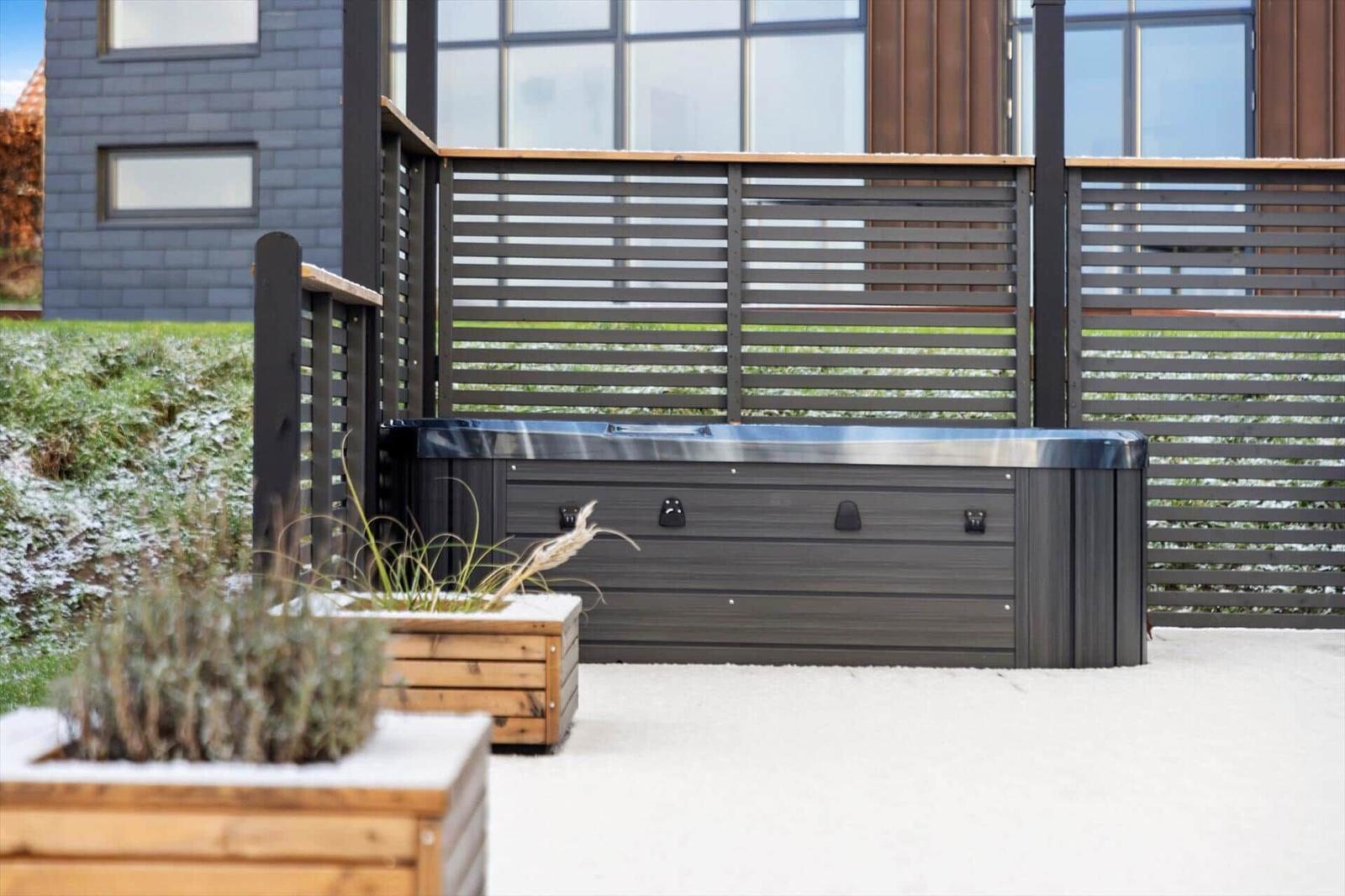 Outdoorwhirlpool mit Holzumrandung und Schneebedeckung im Gartenbereich