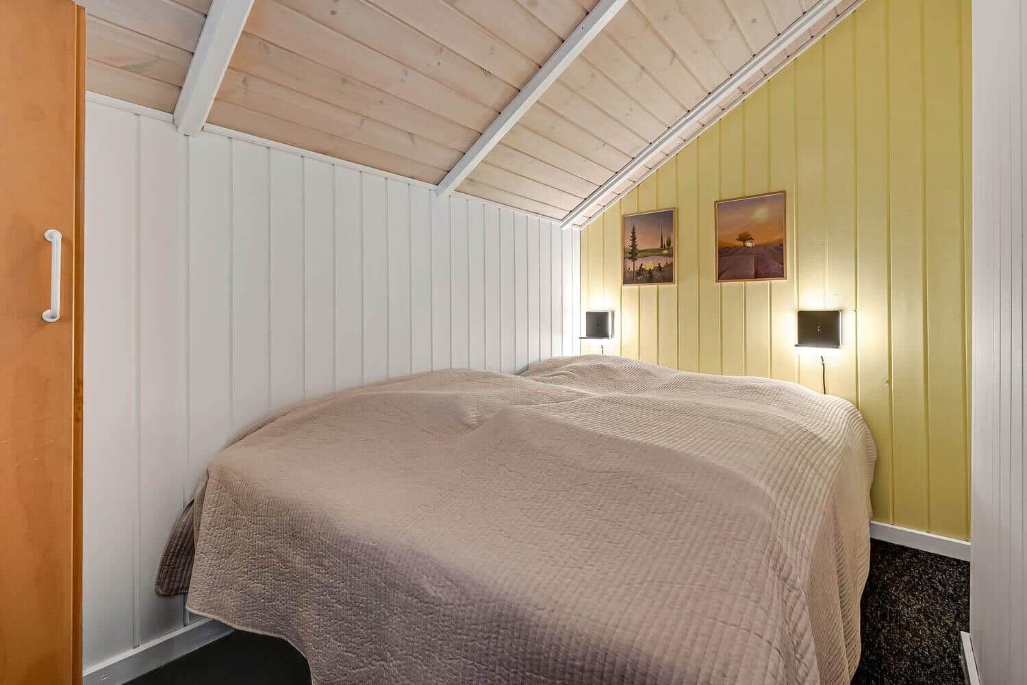 Schlafzimmer mit Bett, gelben Wänden und Holzdecke.
