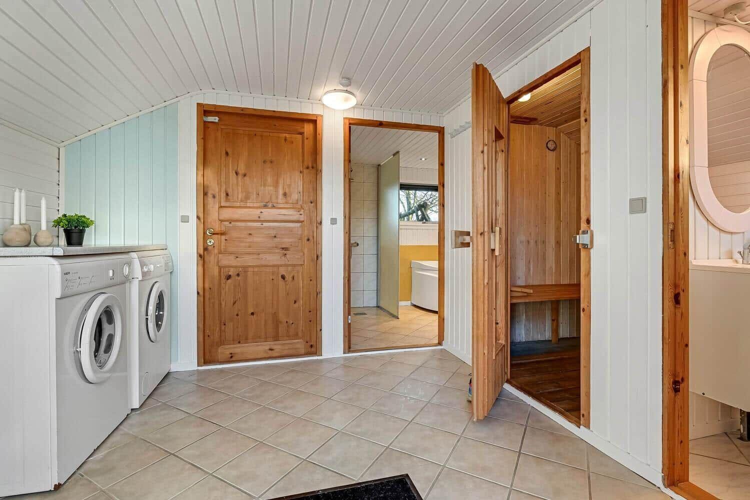 Waschraum mit Sauna und Bad. Holztüren, Fliesenboden und Waschmaschinen.