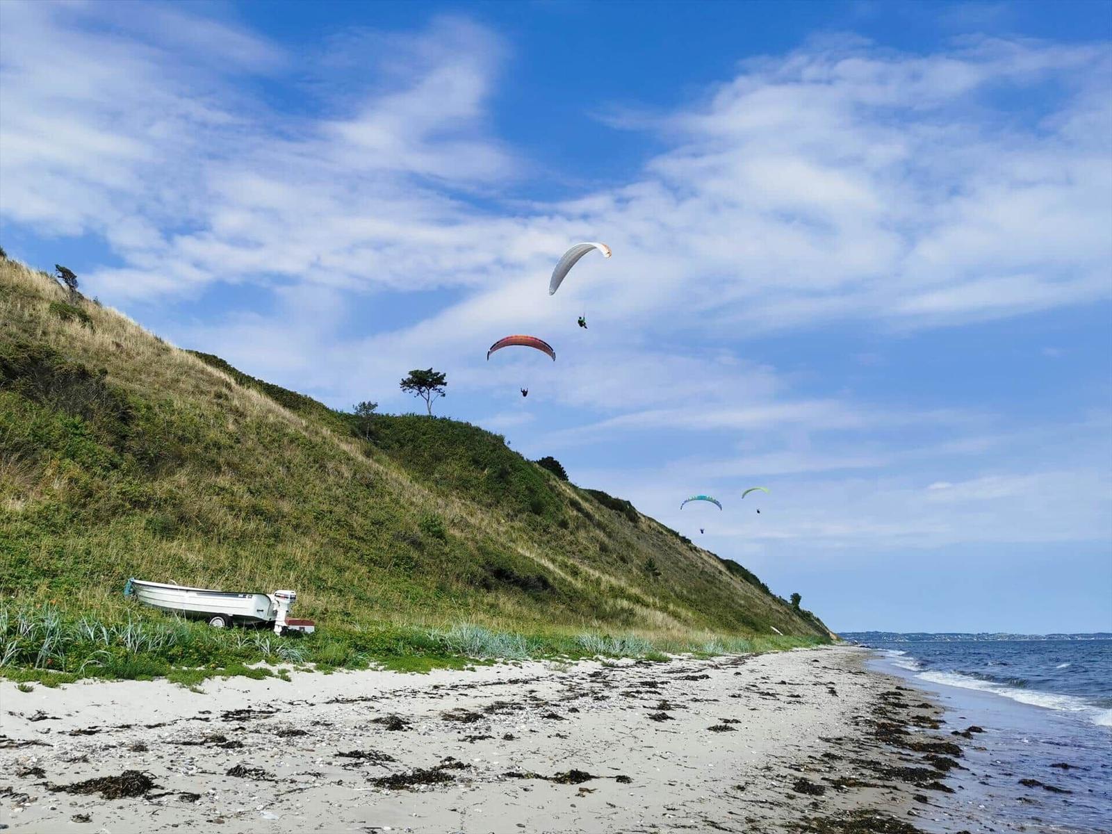 Beach with dunes, paragliders, and a boat.