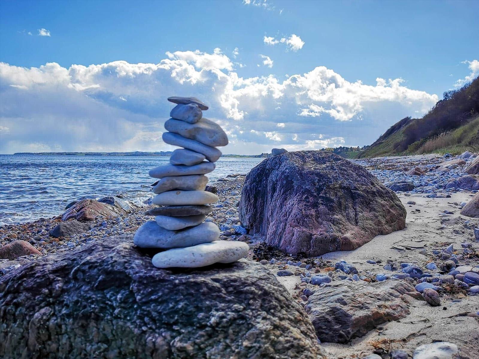 Stone cairn on the beach with view of the sea and cloudy sky.