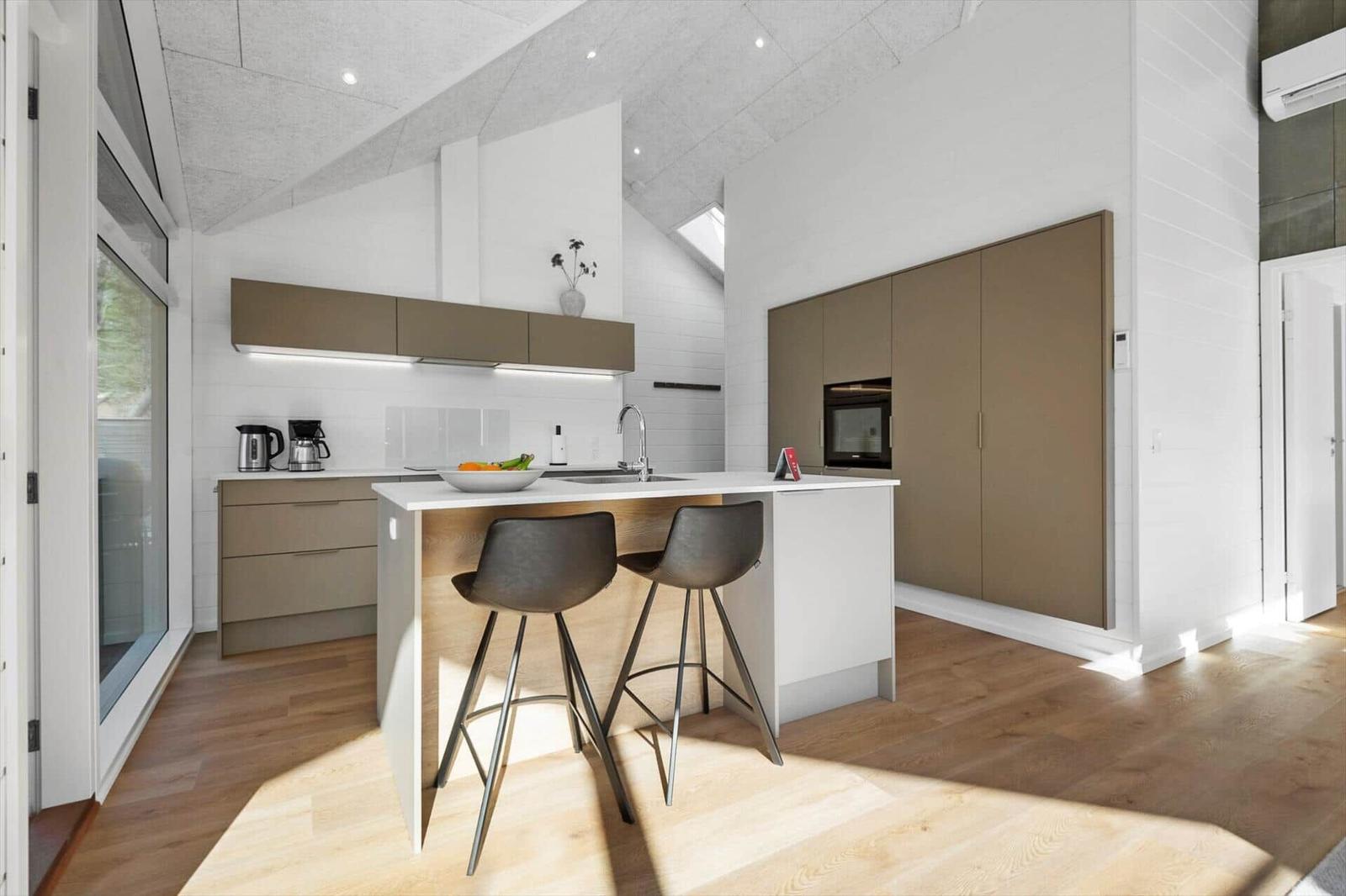 Modern kitchen with island, two bar stools, and built-in oven.