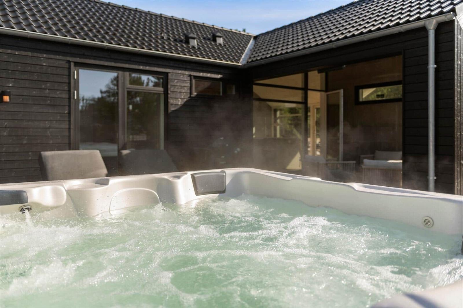 A steaming hot tub in front of a house with dark wood and large windows.