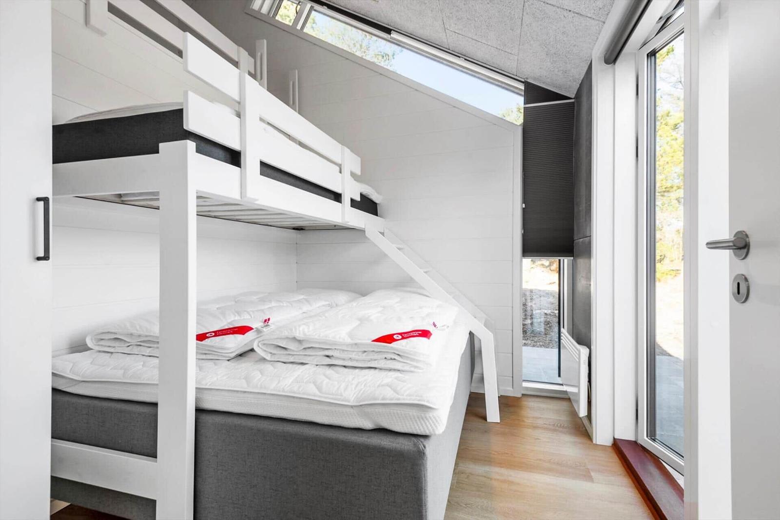 Room with bunk bed, windows, and wooden floor.