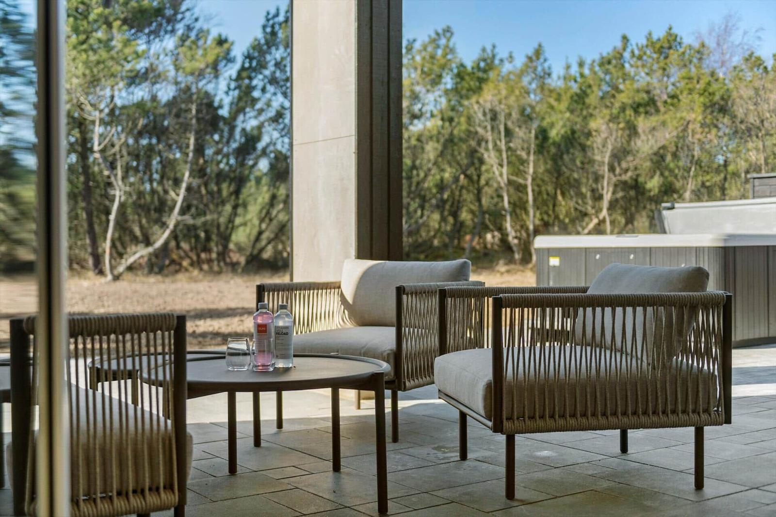 Terrace with seating group, table, and view of forest. Hot tub in background.