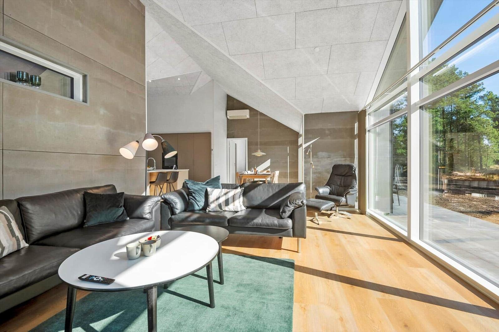 Living area with sofa, seating group, and large window front. Wooden floor and modern furnishings.