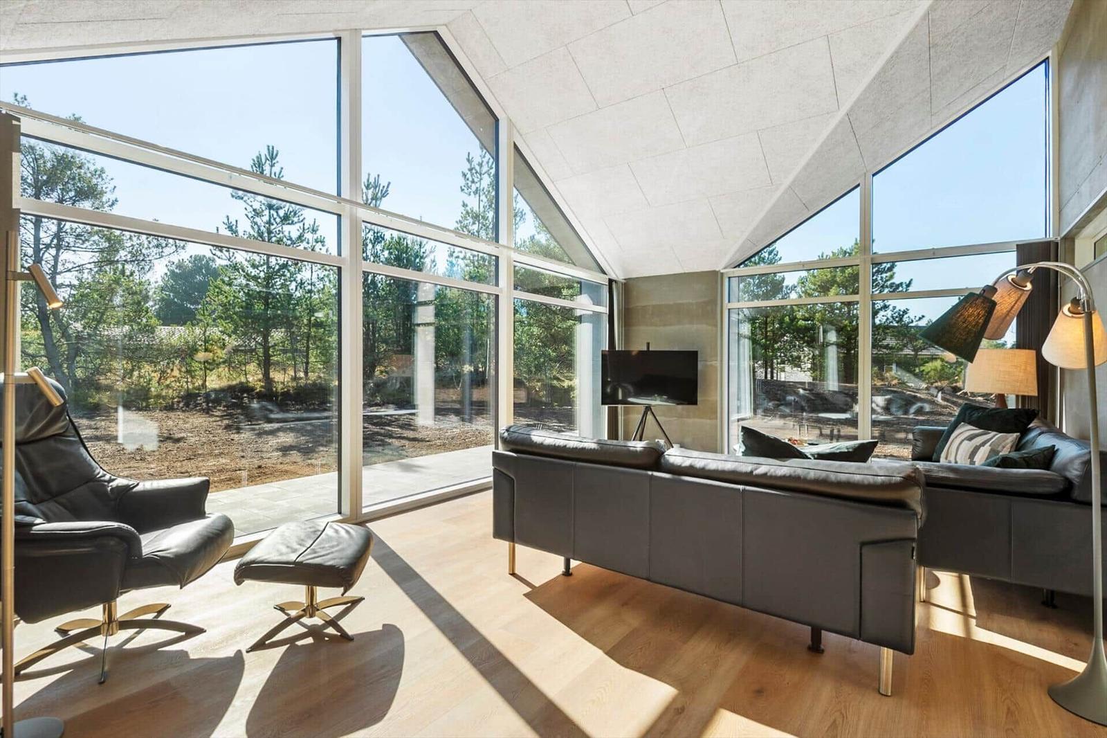 Living room with large windows, sofa and chair. Wooden floor and stone roof.